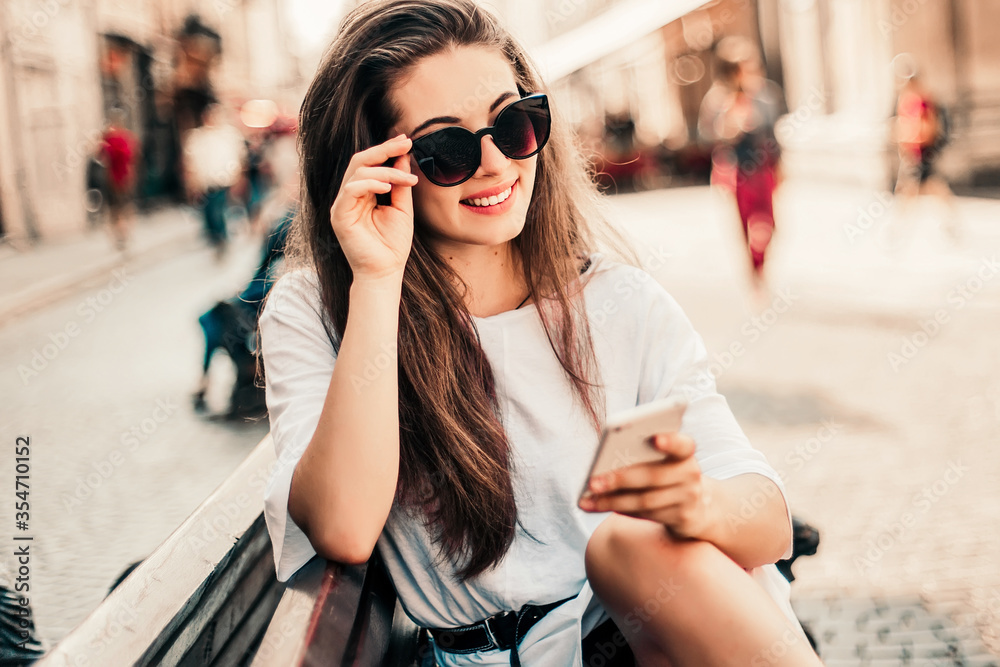 Young stylish woman using phone sitting on the street.