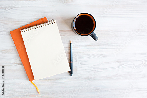 a blank notebook surrounded and coffee cup. orange details, a light wooden background, To-do list, plans, dreams, work from home. Top view,