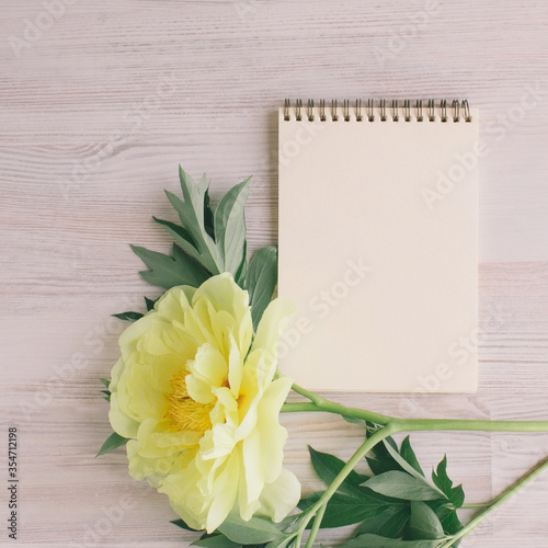 A blank notebook surrounded by yellow peony flower, a light wooden background, To-do list, plans, dreams. Top view, Vintage toned. Copy space for text