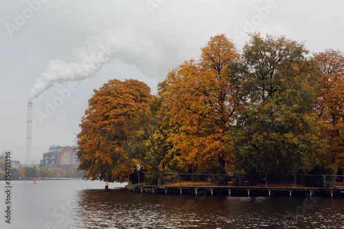 Glimpse of Spree river, near Treptower Park in Berlin, autumnal Chestnut Trees reflected in the water, in the background the smoke  from a factory chimney. photo