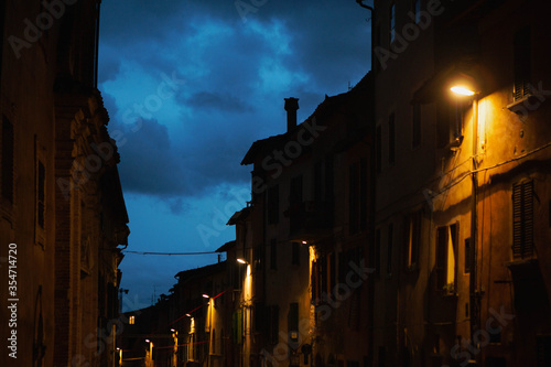 View of a street in the historic center of Perugia at dusk, with houses illuminated by the yellow light of the street lamps that contrasts with the blue of the sky, central Italy, Europe. © Francesca