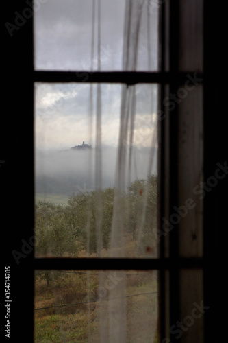 Glimpse of the village of Angello rising from the clouds framed in a window of a country house in the municipality of Magione, Umbrian hills, Central Italy, Europe.