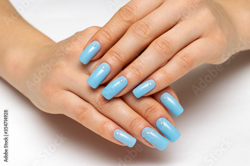 light blue manicure on square long nails with crystals on a white background close-up.