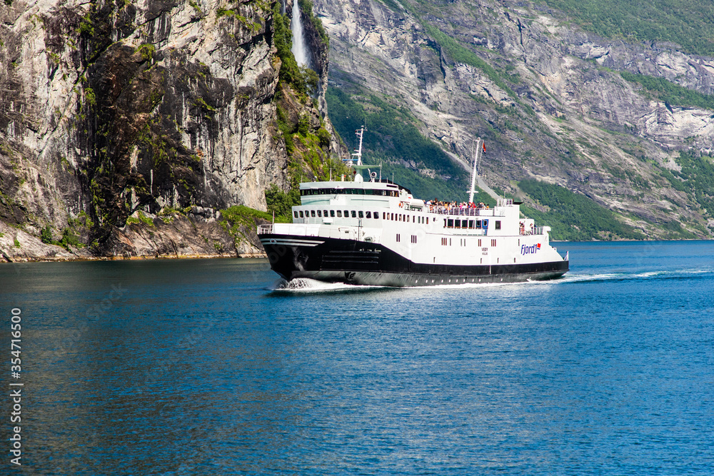 Geiranger, Geirangerfjord, Norway - June , 2019: Touristic ship berry boat floating liner near Geiranger in Geirangerfjorden in summer day. Famous Landmark And Popular Destination. Geiranger, Geirangerfjord, Norway - June , 2019: Touristic ship berry boat floating liner near Geiranger in Geirangerfjorden in summer day. Famous Landmark And Popular Destination.