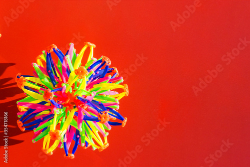 Volumetric multi-colored ball made of plastic sticks on a red background. Top view, flat lay. Abstract geometric shape, copy space, child development, games for children