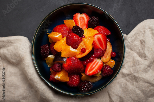 Fresh fruit salad  top view in a bowl on dark concrete background. Vegetarian food concept. Whole food. 