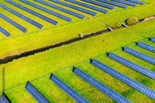 Solar panels of photovoltaic power plant from above with watercourse. Renewable resource of energy