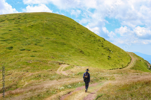 A young man with sombrero, backpack and a walking stick hiking on a curvy, beautiful highlands road © Nikola