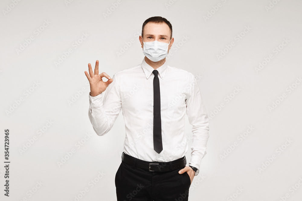 Handsome smiling businessman in facial protective mask showing an ok gesture on the white background, isolated. Mockup for business or healthcare advertising.