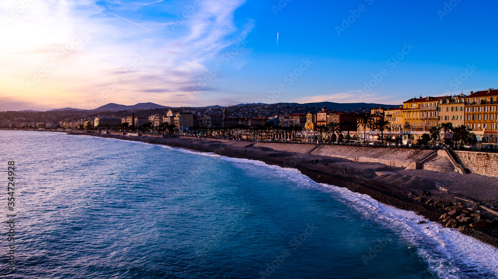 Sunset over the Mediterranean Sea, the public pebble beach and the Promenade des Anglais in Nice, French Riviera, France.