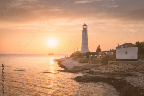 Seascape with a lighthouse on a rocky coast in the rays of the setting sun. Beacon on sunset on the banks of a rocky cape
