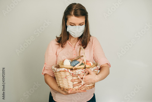 young woman with Easter at the basket and colored eggs she holds in her hands on white backround. quarantine at home in medical surgical masks. Basket, eggs, holiday, coronavirus, illness, stay