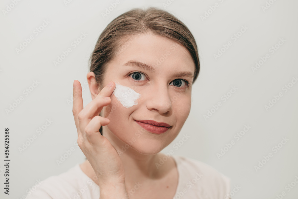 Happy young woman doing beauty treatment. The girl applies white cream on her face on the morning. Happy young woman doing beauty treatment. The girl applies white cream on her face on the morning.