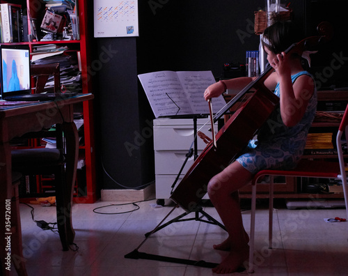 little girl teaching cello from home with computer via video conference