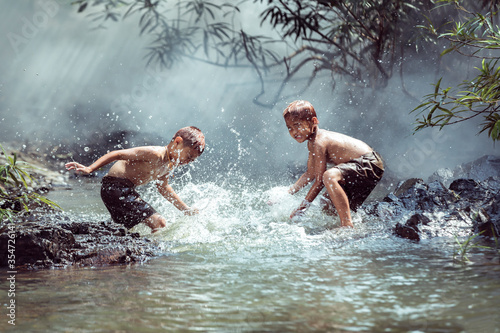 Two boys Happily playing in the water near the stream near their home in the countryside of Thailand