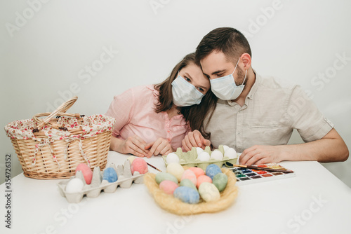 Young white European couple celebrating paint Easter quarantine at home in medical surgical masks. Basket, eggs, holiday, coronavirus, illness, stay home, infection, flue, surgical bandage.