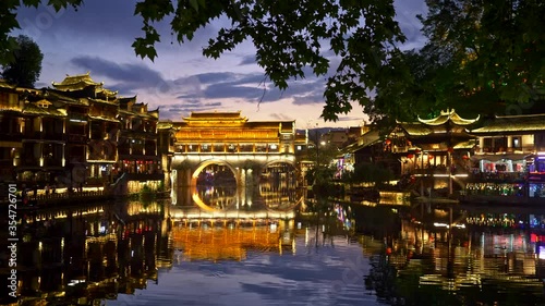 Fenghuang, China. Evening landscape with bright lights illumination. Bridge reflecting on Tuojiang river. People having a good time. Panning shot, UHD photo