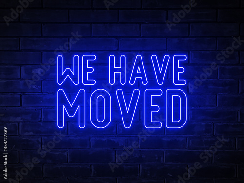 We have moved - blue neon light word on brick wall background