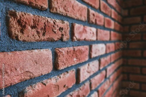 Side angle of a red brick wall corner. Close up view of cracked weathered brickwork material. Modern interior design, unique perspective. Loft like room style at home. Dark street or alleyway outside.