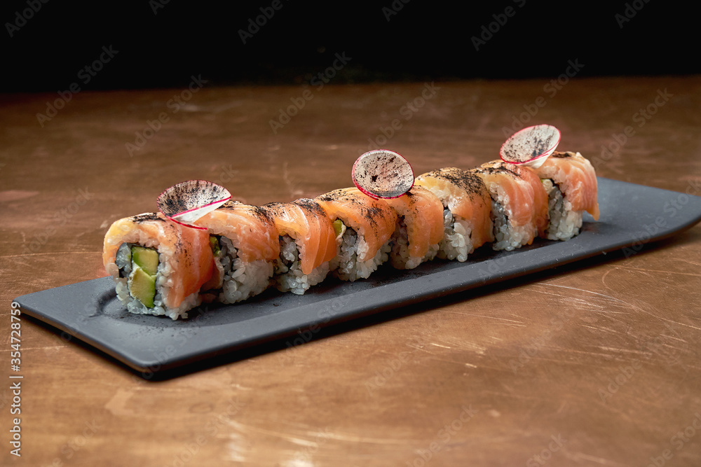 Classic japanese sushi rolls - philadelphia rolls with cream cheese, avocado and salmon on a black plate on a copper, metal background Classic japanese sushi rolls - philadelphia rolls with cream cheese, avocado and salmon on a black plate on a copper, metal background
