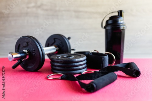 Fototapeta Naklejka Na Ścianę i Meble -  Fitness equipment, green dumbbells and a rubber expander with black handles on a pink background, space for text