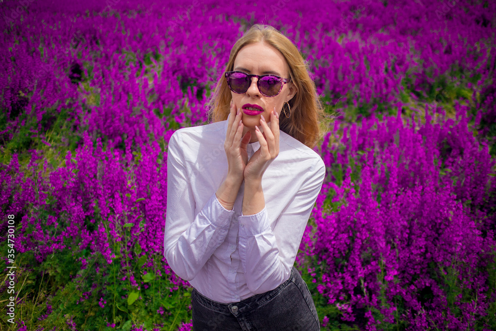blonde in sunglasses and a white shirt on the field with purple flowers blonde in sunglasses and a white shirt on the field with purple flowers