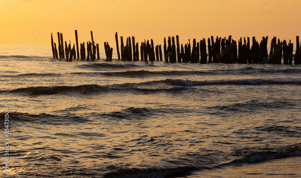 The remains of a wooden pier in the sea in the sunset