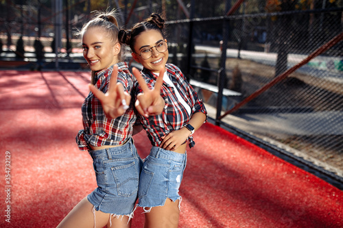 Two stylish young teenage hipster girls showing peace gesture at the stadium. Freedom and Best Friends concept. photo