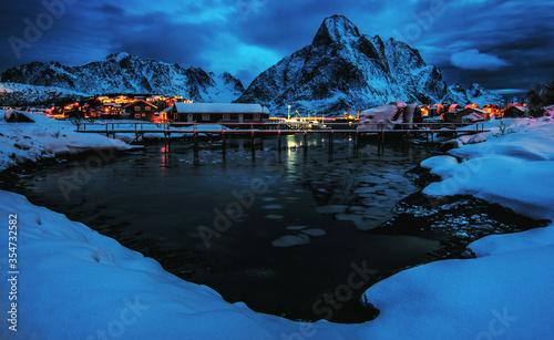 Reine fishing village on Lofoten islands with red rorbu houses in winter with snow in the night. Lofoten islands, Norway.