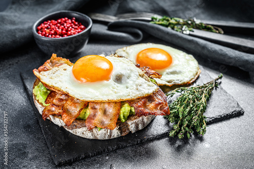 Open sandwich with avocado, fried bacon and egg. Black background. Top view.