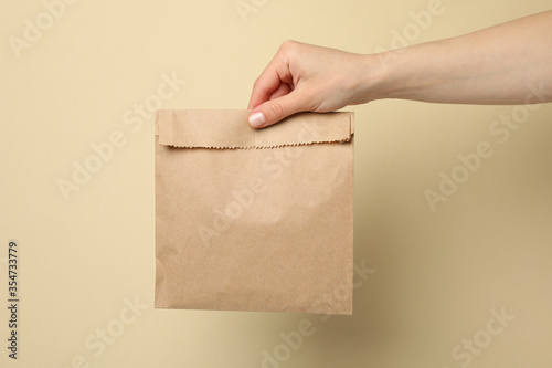 Female hand holding paper bag on beige background, space for text