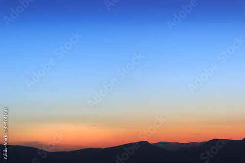 Beautiful, simple deep blue and orange sunset sky and silhouette horizon mountains background