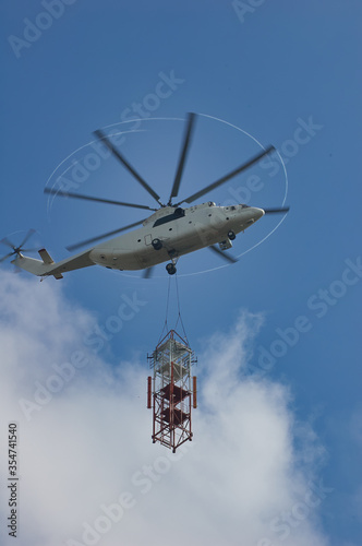 Large transport helicopter carries parts for a construction site. Helicopter in the blue sky with clouds