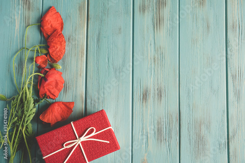 Poppy flowers on a wooden blue background with a gift box. Frame for text with poppies flowers. Flat lay, top view.