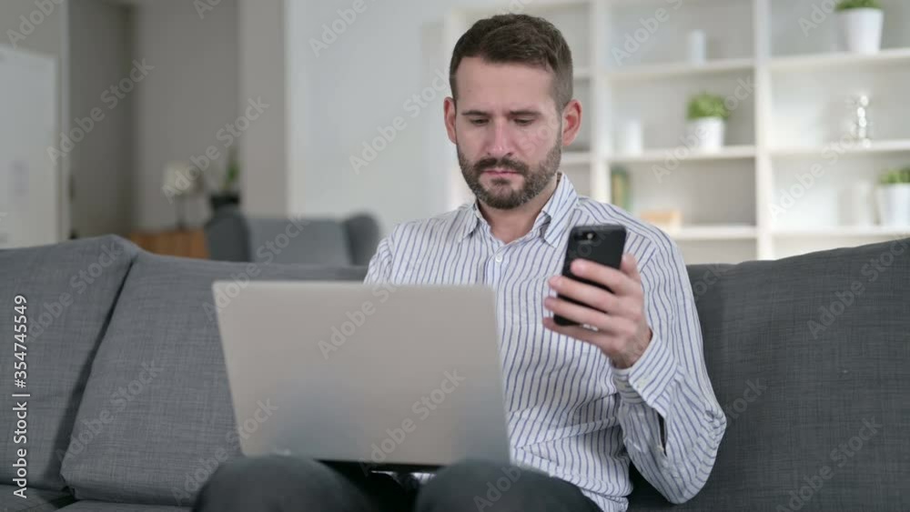 Focused Man working on Smartphone and Laptop at Home Focused Man working on Smartphone and Laptop at Home