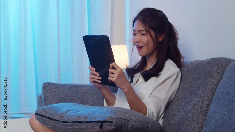 Asian businesswoman using tablet talk to colleagues about plan in video call while working from home at living room at night. Self-isolation, social distancing, quarantine for coronavirus prevention.