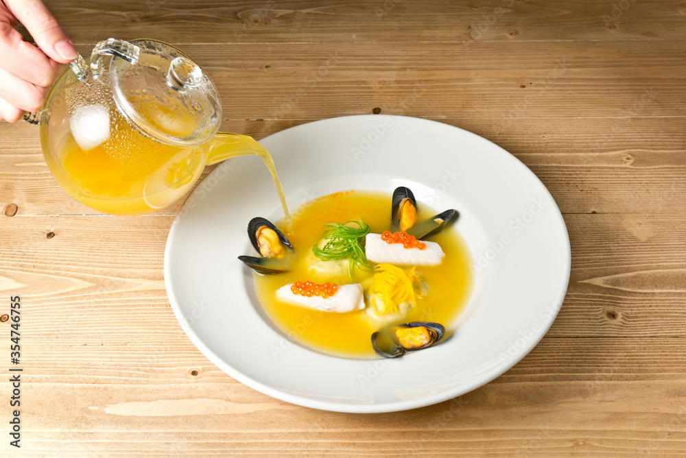 Soup with mussels and spring rolls with caviar. On a white plate. On a rustic wooden background Soup with mussels and spring rolls with caviar. On a white plate. On a rustic wooden background