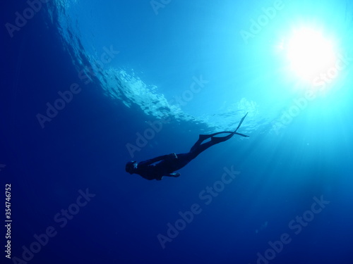 free diver apnea woman underwater blue water with sun beams and rays