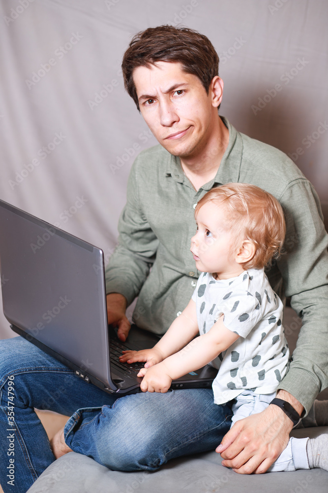 young man working at home with a laptop with a baby on his hands. Stay home concept. Home office with kids. young man working at home with a laptop with a baby on his hands. Stay home concept. Home office with kids.
