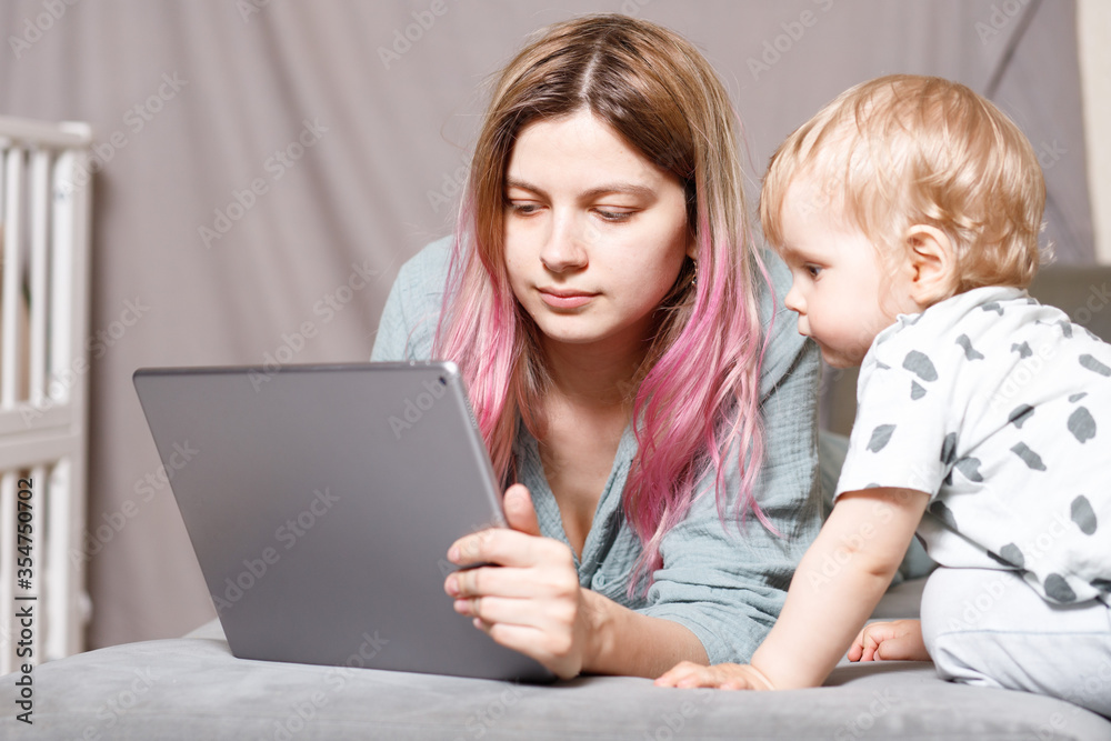 A young woman works at home with a tablet computer, along with a child.the son wants to communicate with his mother, they make noise and interfere with work.isolation during the coronovirus pandemic A young woman works at home with a tablet computer, along with a child.the son wants to communicate with his mother, they make noise and interfere with work.isolation during the coronovirus pandemic