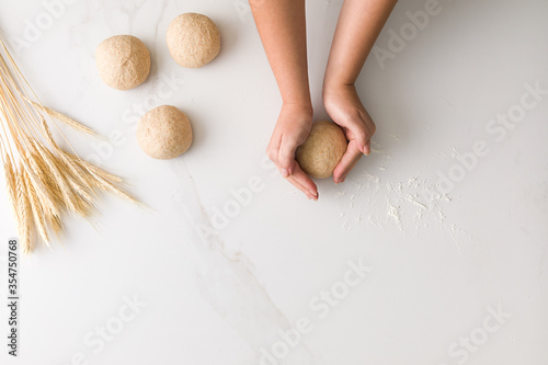 Top view of female hands molding bread dough in a marble table with three molded bread dough, wheat and flour with space for text