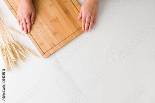 Top view of female hands resting in a wooden board in a marble table with wheat and flour with space for text