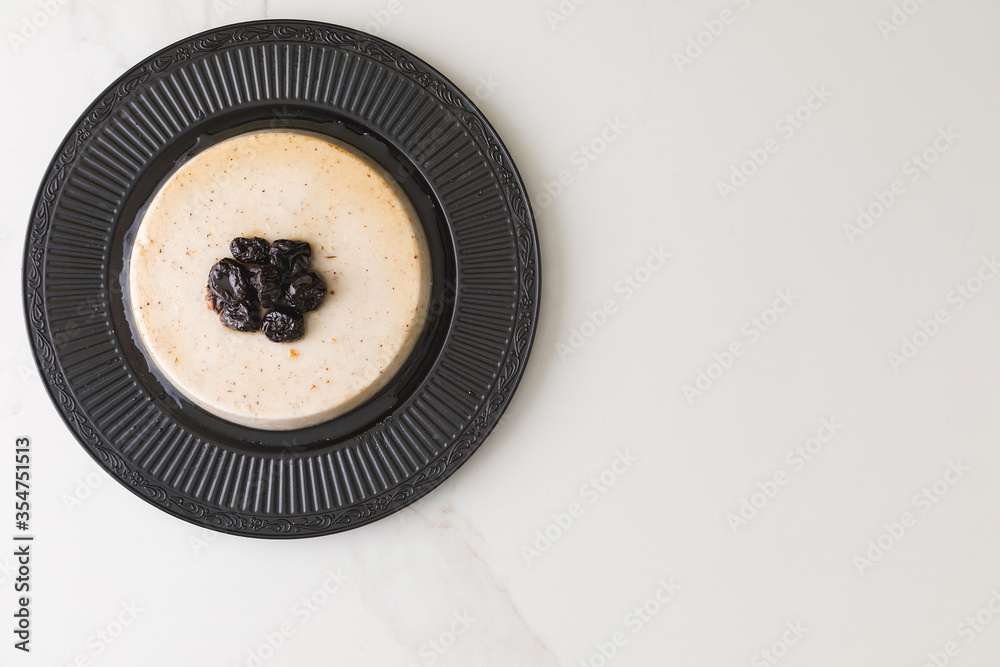 Top view of a coconut pudding with plums in a black plate in a marble table and space for text (2) Top view of a coconut pudding with plums in a black plate in a marble table and space for text (2)