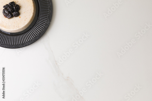 Top view of a coconut pudding with plums in a black plate in a marble table and space for text (3)