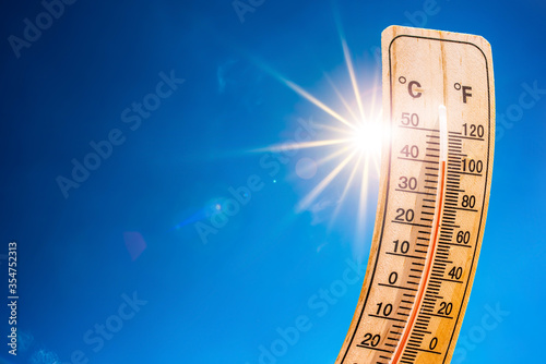 Concept or background for a heat wave or global warming, blue summer sky with with bright sun and thermometer