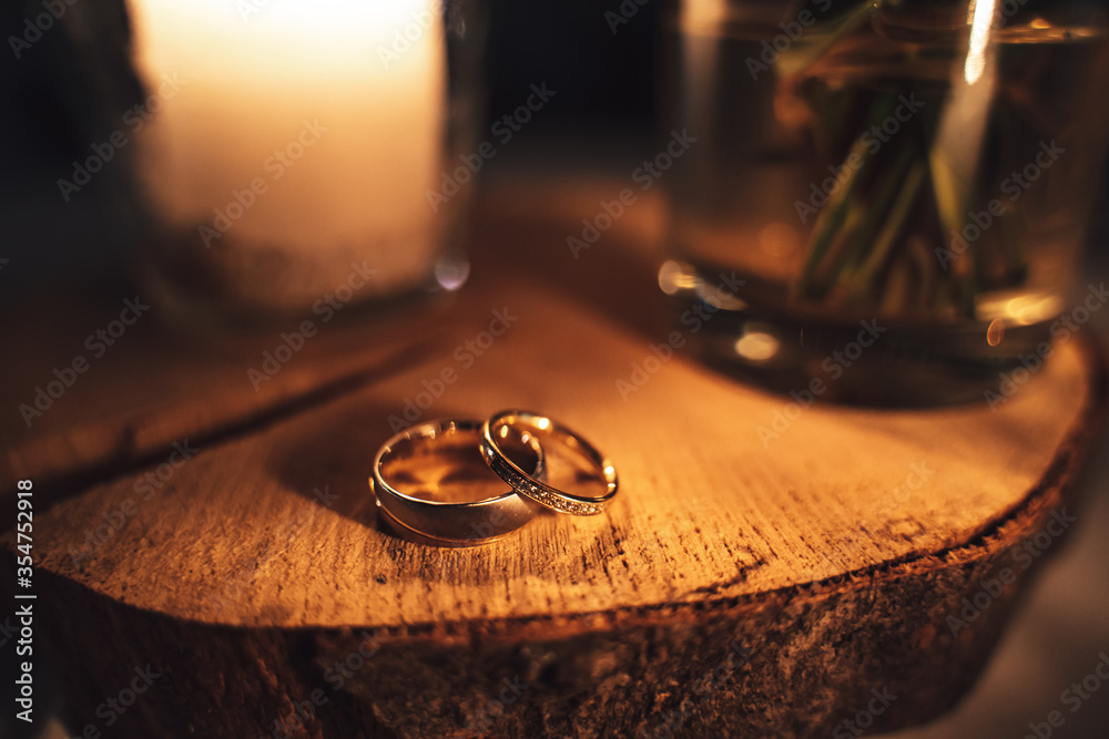 Pair of decorated wedding rings laying on wood. Warm tones by candle light. Shallow depth of field. Orange toned. Pair of decorated wedding rings laying on wood. Warm tones by candle light. Shallow depth of field. Orange toned.