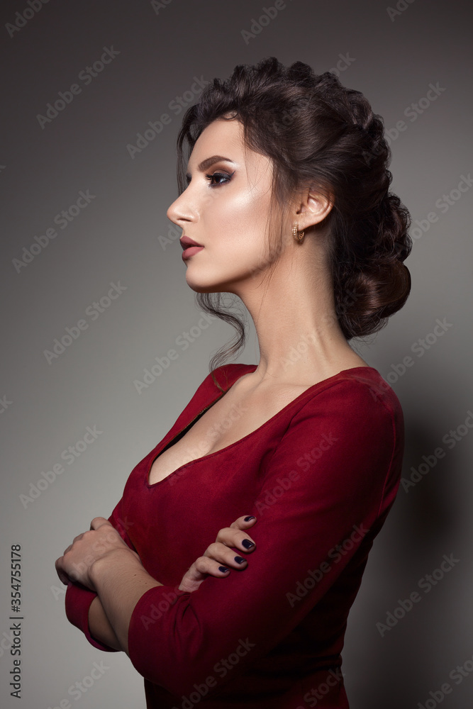 Beautiful woman with stylish haircut and big earrings looking down over shoulder, touching neck by hand. Brunette girl posing in dark studio, wearing red dress, with evening make up and long eyelashes Beautiful woman with stylish haircut and big earrings looking down over shoulder, touching neck by hand. Brunette girl posing in dark studio, wearing red dress, with evening make up and long eyelashes