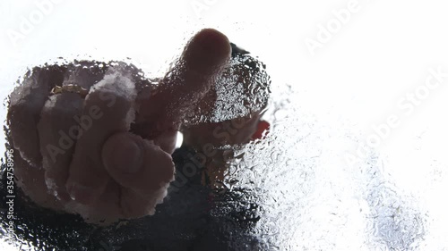 High quality close-up 4k slow motion video of a man drawing heart shape on a wet glass with his pointing finger on a white blurred background of a blue cloudy sky. Abstract footage with a copy space