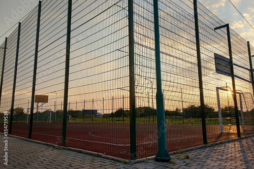 Outdoors mini football and basketball court with ball gate and basket surrounded with high protective fence.