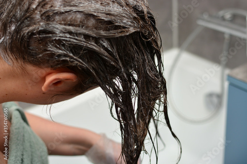 Young woman dyes her hair at home. The girl coloring her hair in her own bathroom. Quarantine, home hair care, stay at home concept.